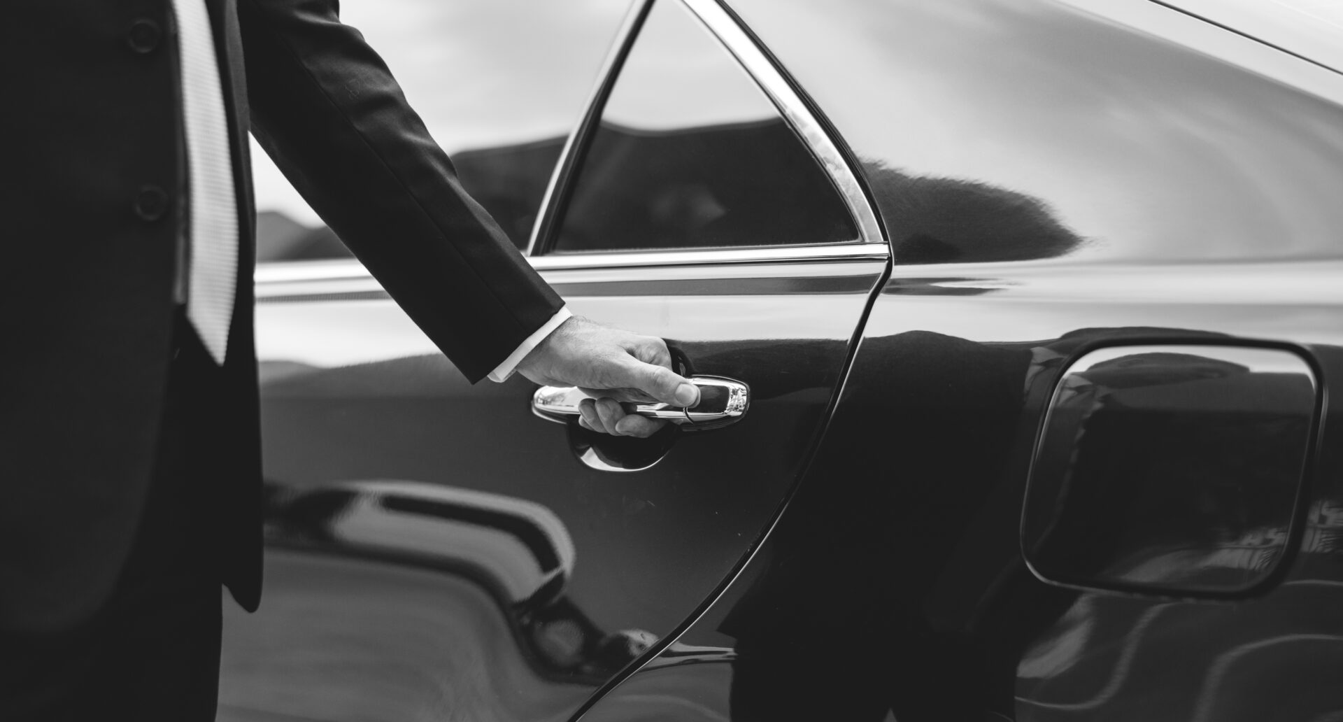A chauffeur opening the rear door of a black saloon